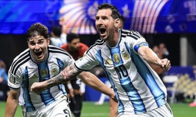 Two Argentina national team football players celebrate on the pitch, arms raised and shouting in blue-and-white striped jerseys with the number 10 visible on one shirt.