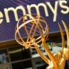 Golden Emmy statuette raised above the head with a purple display reading 'emmys' in the background.