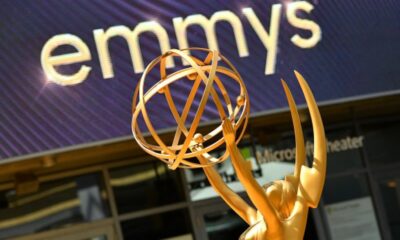 Golden Emmy statuette raised above the head with a purple display reading 'emmys' in the background.