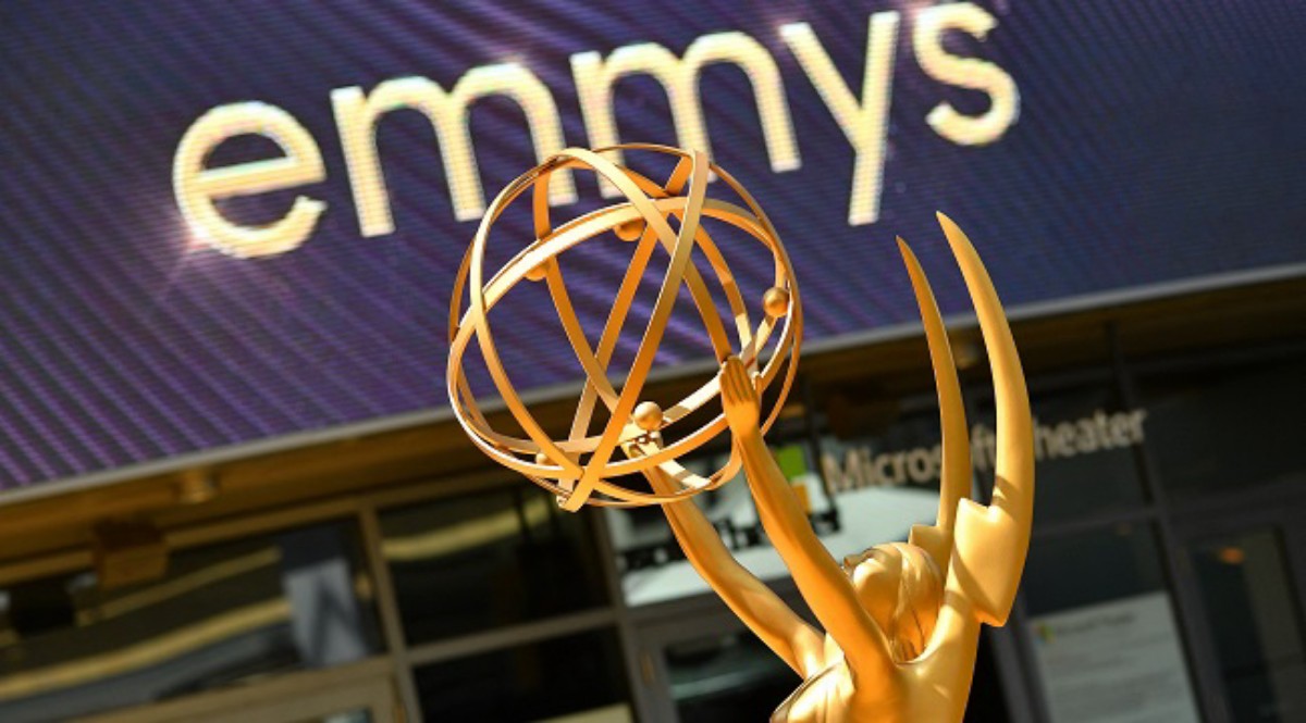 Golden Emmy statuette raised above the head with a purple display reading 'emmys' in the background.