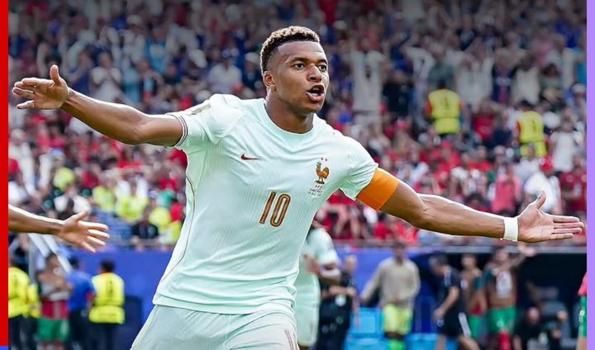 France captain wearing a light blue jersey with number 10, arms outstretched in celebration on the pitch, crowd in the stadium behind him.