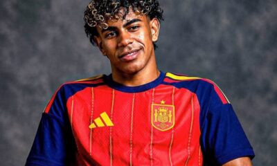 Young man wearing a red Spain national team soccer jersey, smiling against a dark backdrop.
