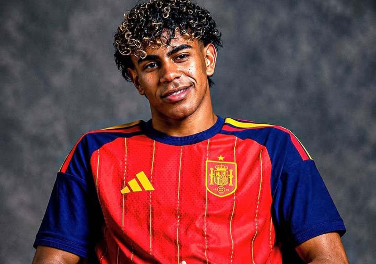 Young man wearing a red Spain national team soccer jersey, smiling against a dark backdrop.