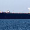 Large bulk carrier with dark hull and white superstructure sailing on blue ocean.