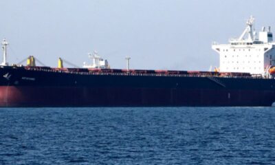 Large bulk carrier with dark hull and white superstructure sailing on blue ocean.