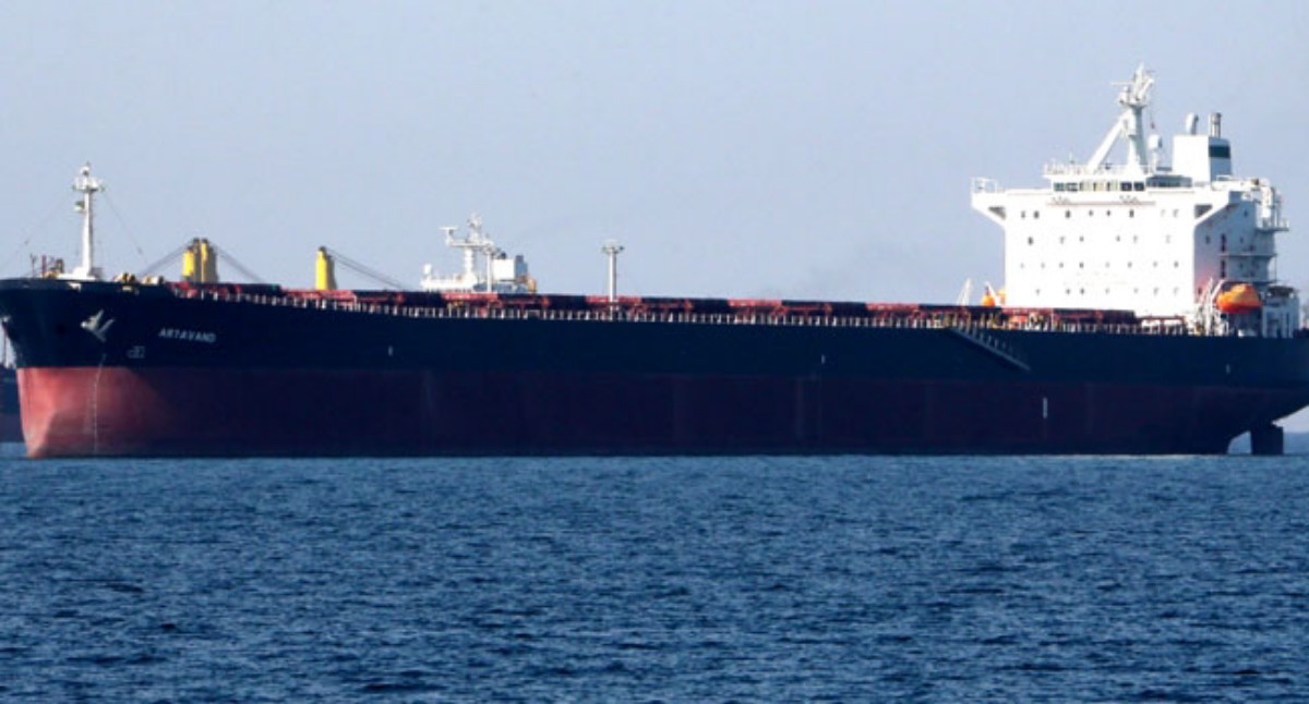Large bulk carrier with dark hull and white superstructure sailing on blue ocean.