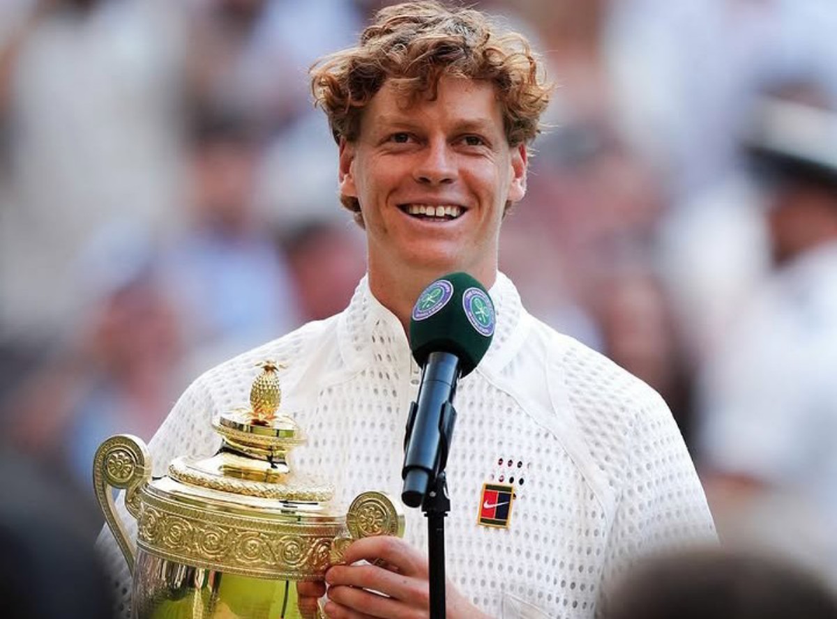 Wimbledon champion smiling while holding the ornate trophy and speaking into a microphone