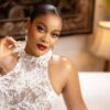 Elegant woman wearing a white lace high-neck dress with pearl embellishments and bold red lipstick, posing on a sofa.