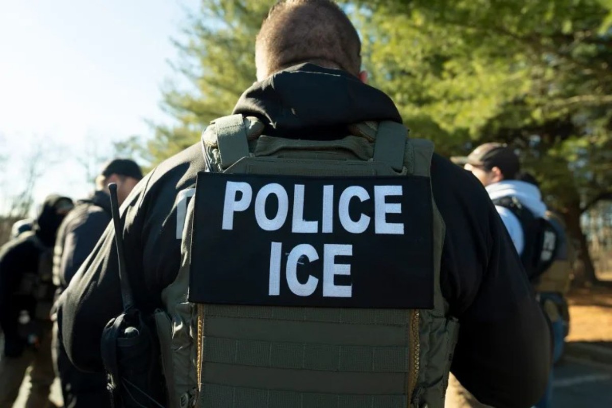 Back view of a uniformed officer wearing tactical gear with a bold 'POLICE ICE' patch on the vest (informative security context).