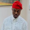 Man wearing a red fez-style hat and white patterned shirt, posing indoors.