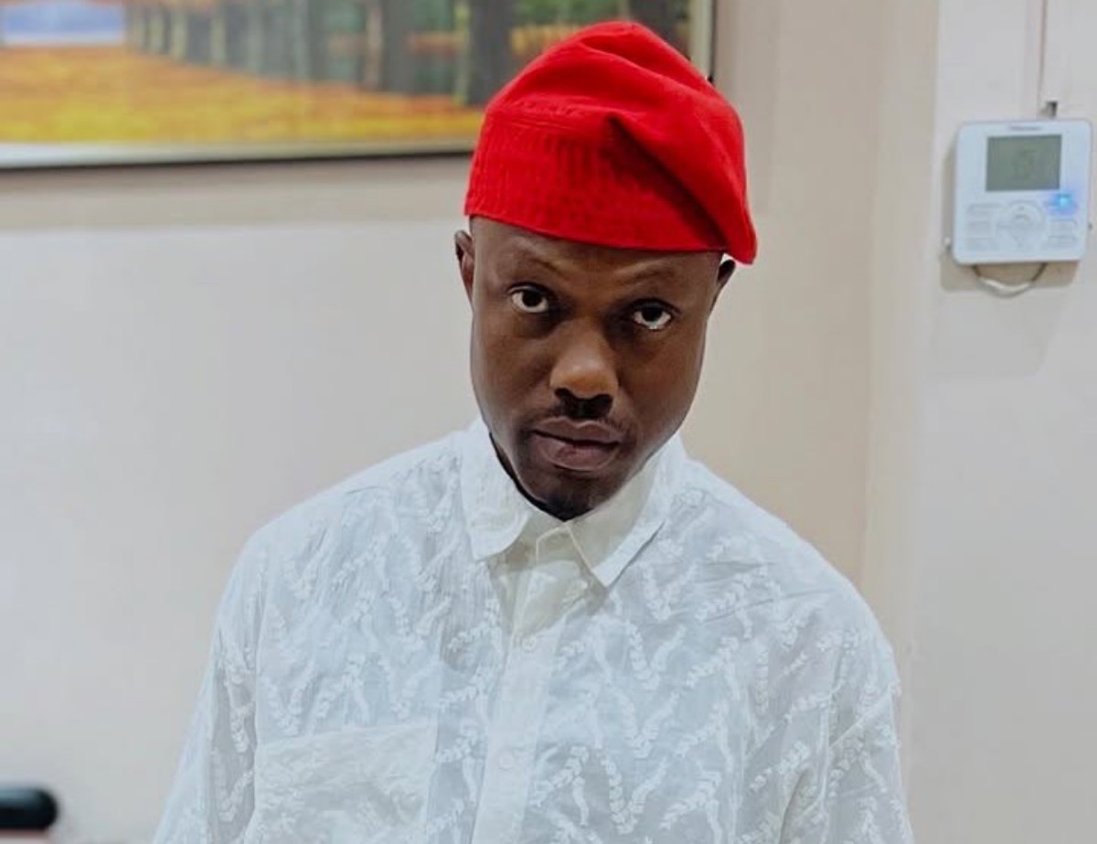 Man wearing a red fez-style hat and white patterned shirt, posing indoors.