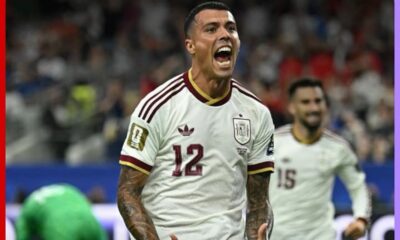 Spain national team footballer in a white kit (number 12) celebrates a goal with his mouth open, on a crowded field.”