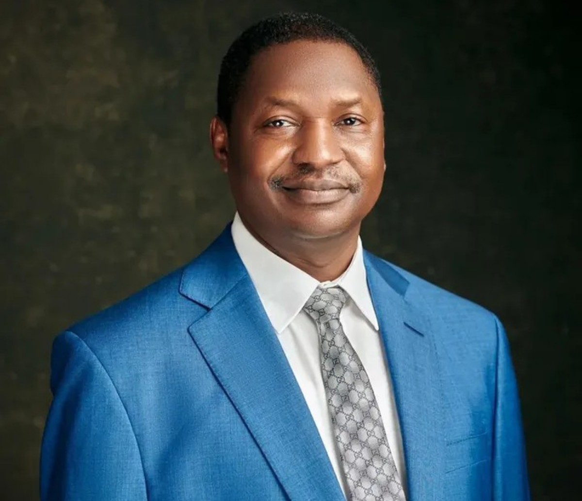 Portrait of a man in a blue suit and gray patterned tie against a dark studio backdrop.