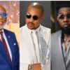 Three men in fashionable suits wearing sunglasses: left in blue suit and bright blue round glasses, smiling; center in white suit with patterned scarf and dark sunglasses; right in gray suit with a beard and aviator-style sunglasses.