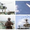 Navy helicopter hovering above a carrier deck with crew and equipment nearby.