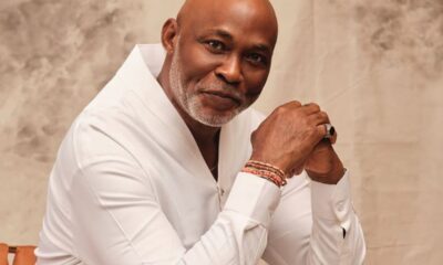 Portrait of a bald, bearded man in a white shirt, clasping his hands and looking at the camera with a gentle smile.