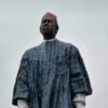 Large statue of an African man in a blue robe and red fez against a cloudy sky