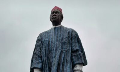 Large statue of an African man in a blue robe and red fez against a cloudy sky