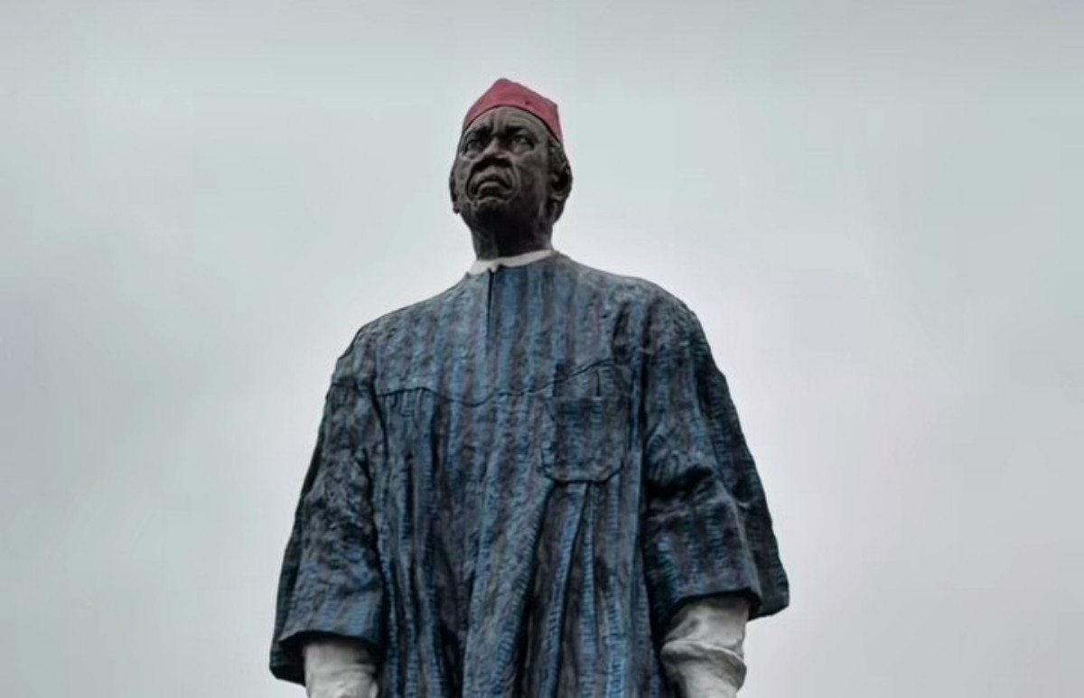 Large statue of an African man in a blue robe and red fez against a cloudy sky
