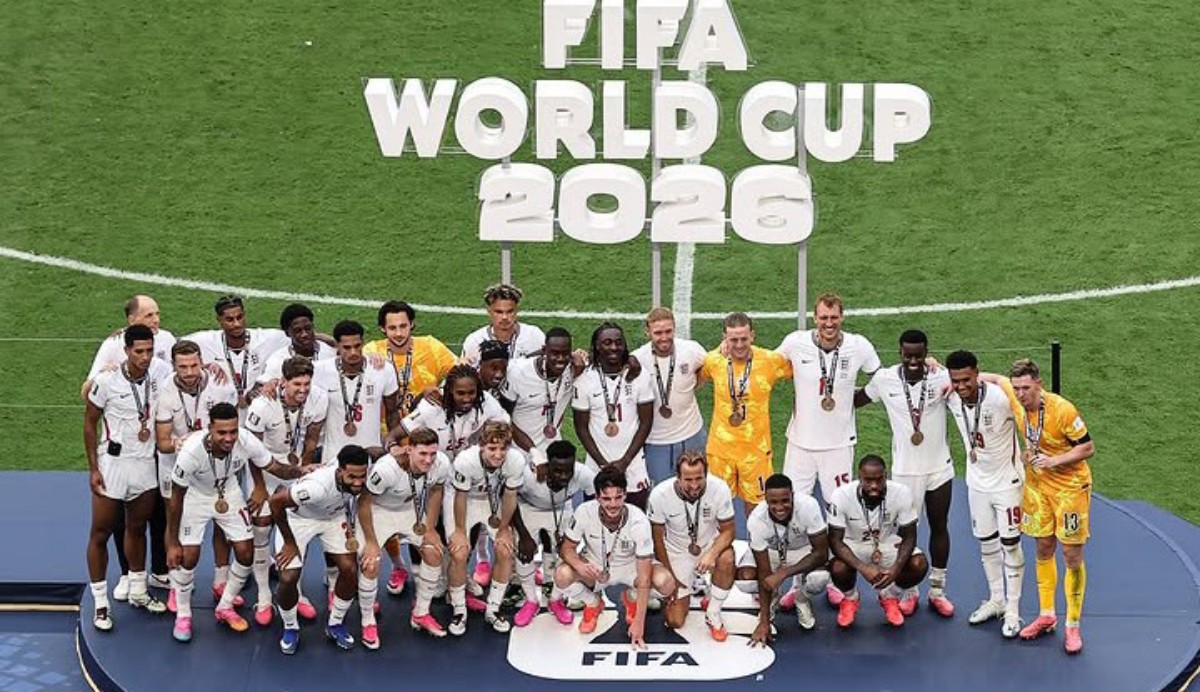 Soccer team posing on a podium with medals after winning the FIFA World Cup 2026 on a grass field.