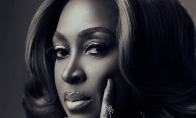Black-and-white close-up portrait of a woman with glamorous makeup, touching her cheek with a jeweled finger.