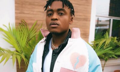 Young man posing outdoors in a pastel color-block jacket with a heart patch, looking at the camera.