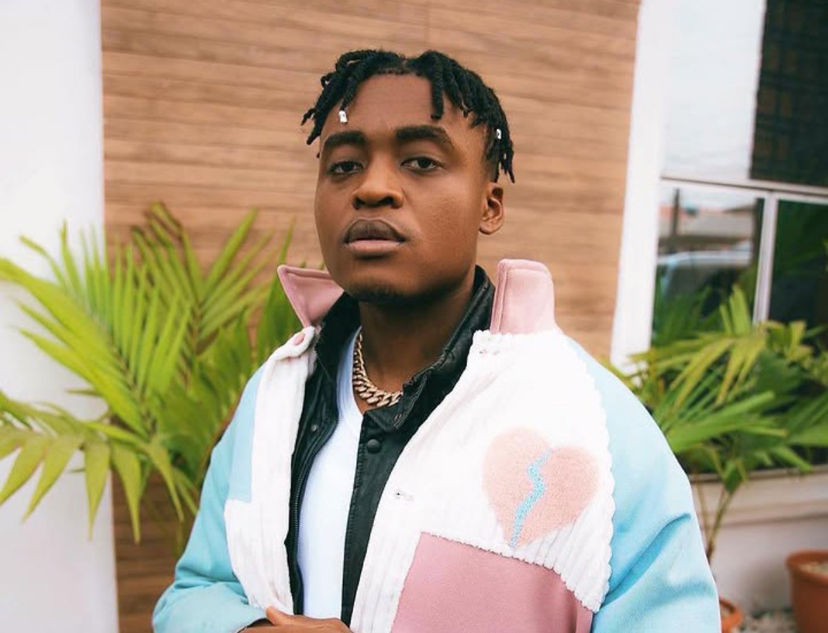 Young man posing outdoors in a pastel color-block jacket with a heart patch, looking at the camera.