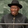 Man wearing a black hat and traditional black robe speaks at a podium with two microphones.