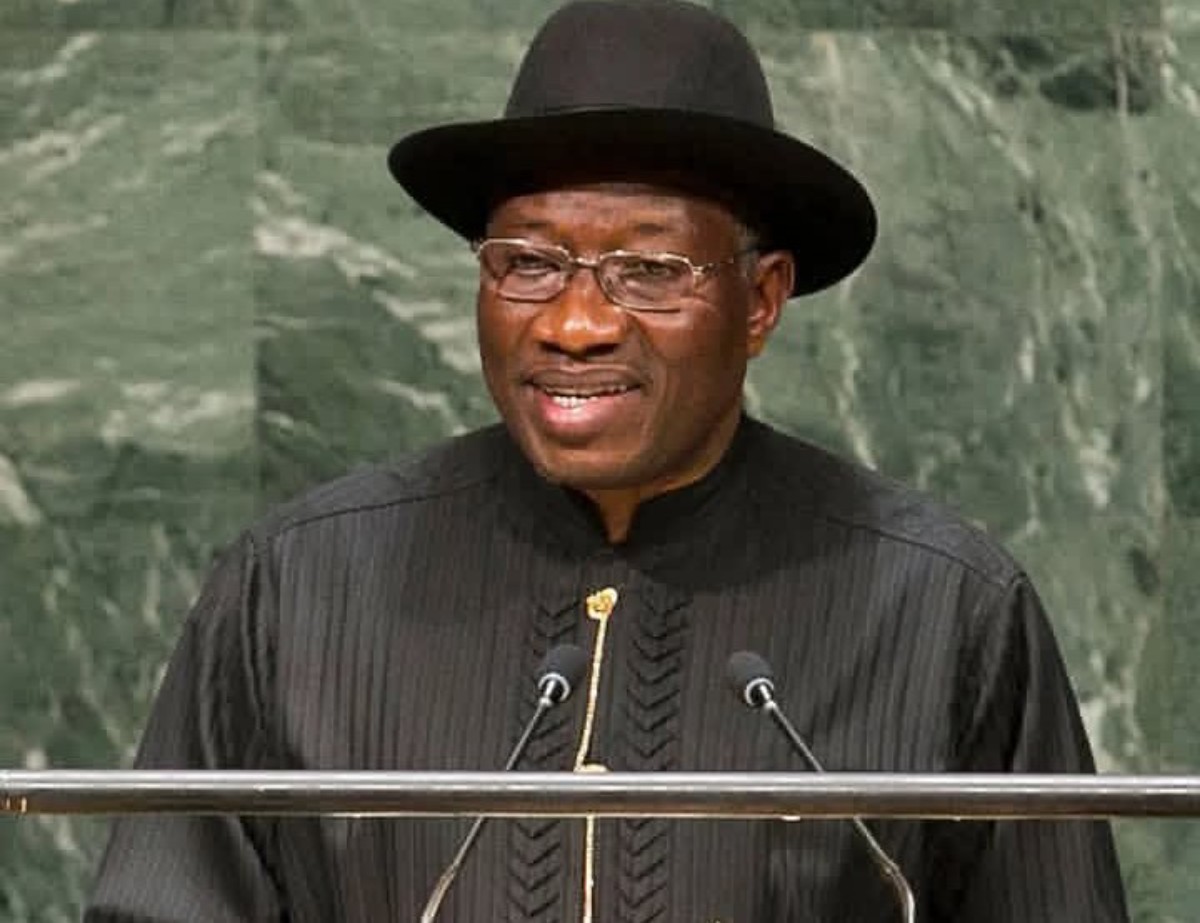 Man wearing a black hat and traditional black robe speaks at a podium with two microphones.