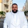 Man with a full beard in a white suit with a sparkling vest standing in a sunny residential street.