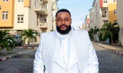 Man with a full beard in a white suit with a sparkling vest standing in a sunny residential street.