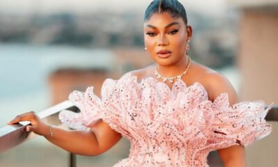 Woman in a pink sequined off-shoulder dress standing on a balcony, looking at the camera.