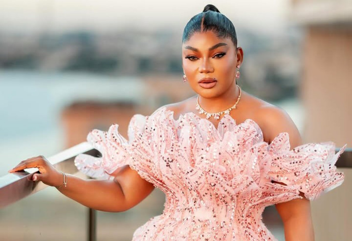 Woman in a pink sequined off-shoulder dress standing on a balcony, looking at the camera.