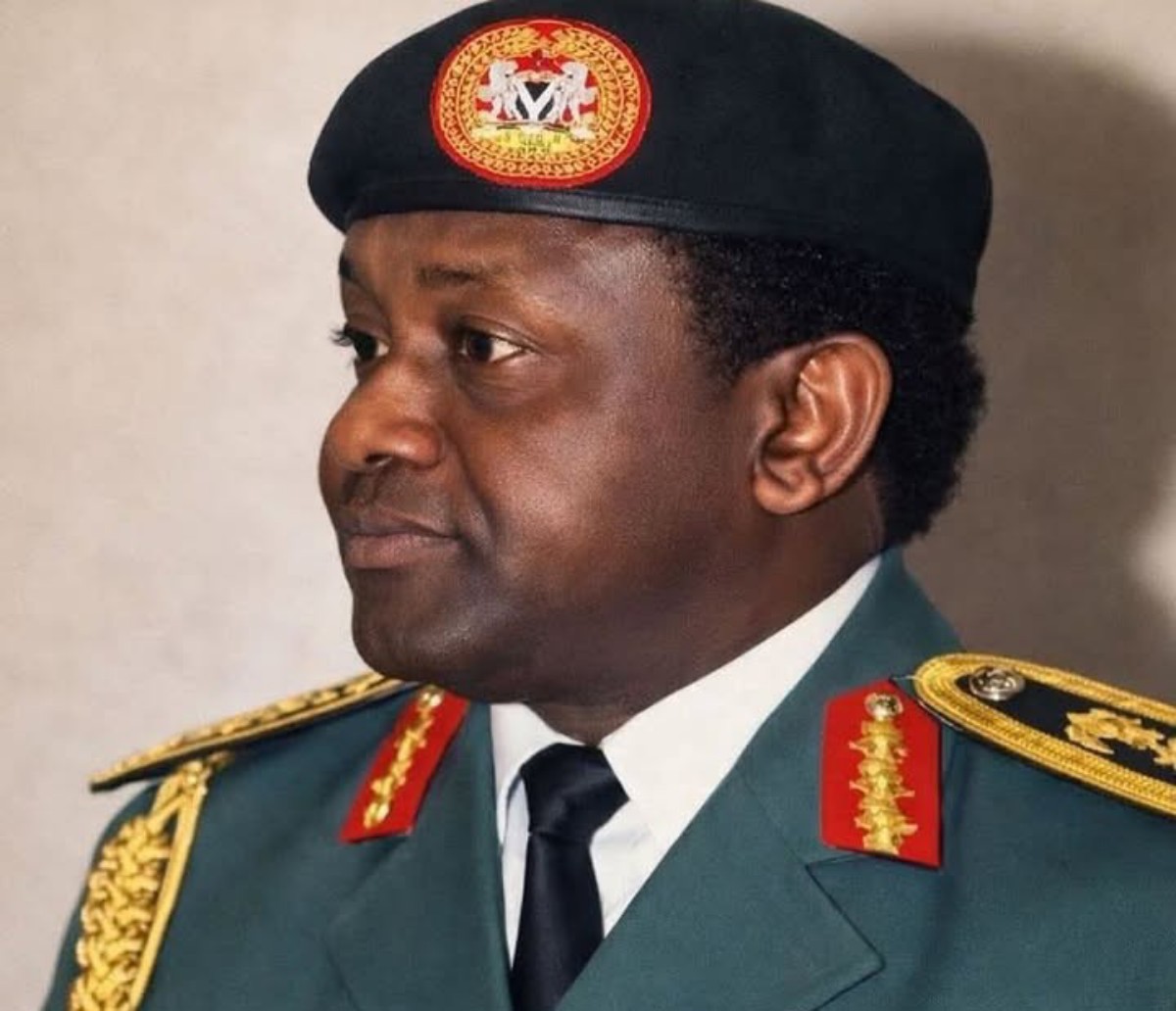 Profile view of a Black male military officer in ceremonial dress blues/greens, with gold shoulder insignia, red collar patches, and a black beret bearing an emblem, looking to the left.