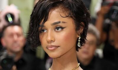 Young woman with short wet-look hair, diamond teardrop earrings, and a gold necklace at a red-carpet event.