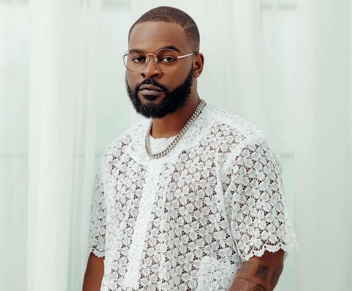 Portrait of a man with a trimmed beard and glasses wearing a white lace shirt and a silver chain.