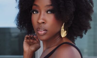 Portrait of a Black woman with natural curly hair, wearing a black sleeveless top and large gold earrings, looking at the camera.