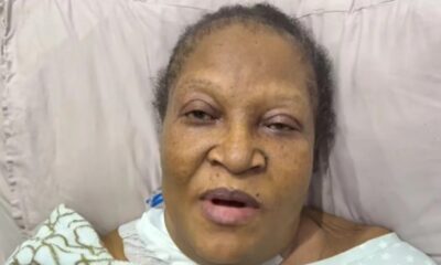 Older Black woman lying in bed propped on a pillow, mouth slightly open and eyes tired, wearing a light hospital gown and blanket nearby.