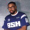 Man with glasses wearing a blue ASH jersey with the number 18, posing against a gray backdrop.