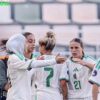 Group of women soccer players in white and green celebrate on the field; a large vertical 'TEAM' text appears on the left.