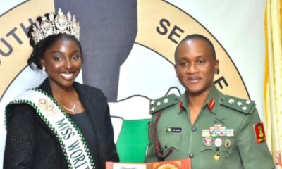 Miss World contestant wearing a crown and sash beside a decorated military officer at a ceremony.