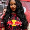 Portrait of a young woman with long wavy black hair wearing a Red Bull jersey with red lightning pattern, outdoors in a crowd experience set.