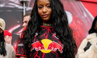 Portrait of a young woman with long wavy black hair wearing a Red Bull jersey with red lightning pattern, outdoors in a crowd experience set.