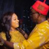 Couple dancing closely at a celebration: woman in a gold lace dress facing a man in a bright yellow traditional outfit and red hat.