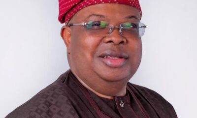 Smiling man in a brown traditional outfit with a red patterned cap and glasses, head-and-shoulders portrait.