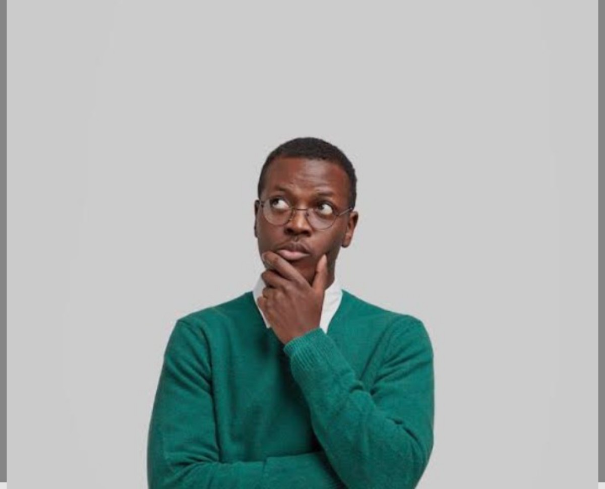 Man in a green sweater with glasses rests his chin on his hand, appearing thoughtful against a light gray background.