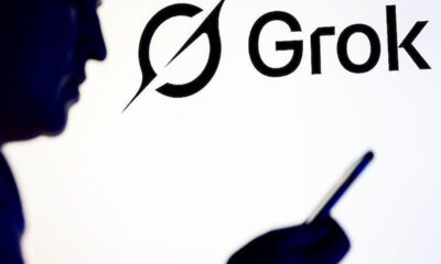Silhouetted person holding a smartphone beside a large Grok logo in the background.