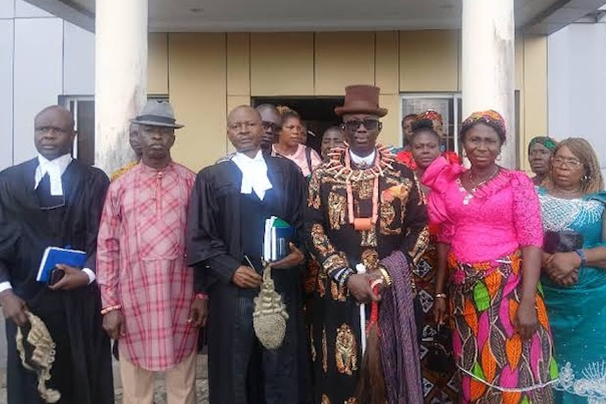 Group of adults posing outside a building in formal attire; central man wears an ornate patterned suit and top hat.3Aefte 0:00:01