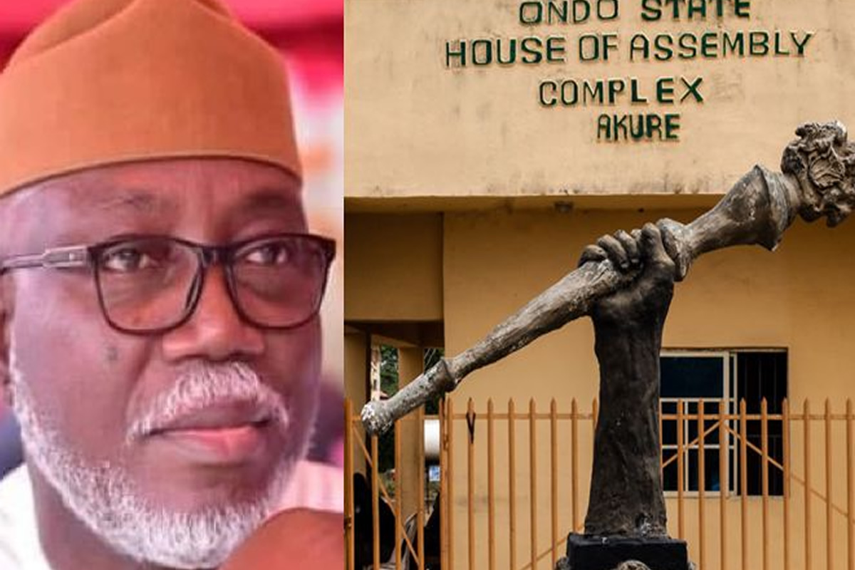 Portrait of a man wearing glasses and a brown cap, next to a bronze statue holding a torch in front of the Ondo State House of Assembly Complex, Akure, Nigeria.