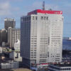 Tall grey skyscraper with a red UBA sign on top, part of a city skyline with water in the distance.